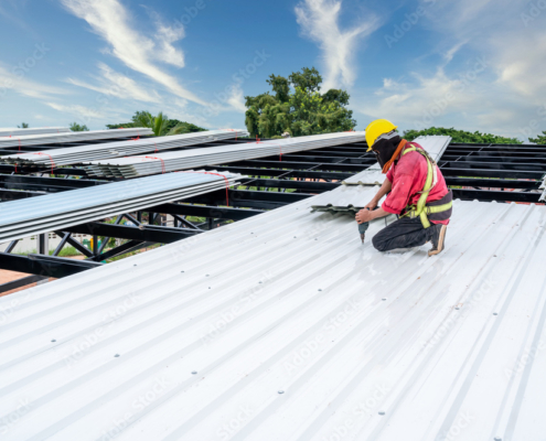 A Roofer Construction worker install new roof, Electric drill used on new roofs with white Metal Sheet. Working at height equipment. Fall arrestor device for worker.