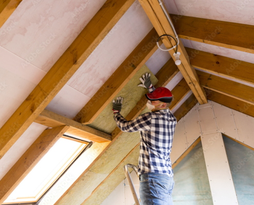 Man installing thermal roof insulation layer  - using mineral wool panels. Attic renovation and insulation concept