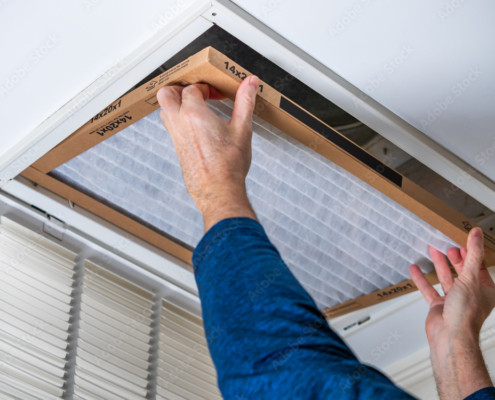 Man replacing dirty HVAC air filter in ceiling vent. Home air duct system maintenance for clean air.