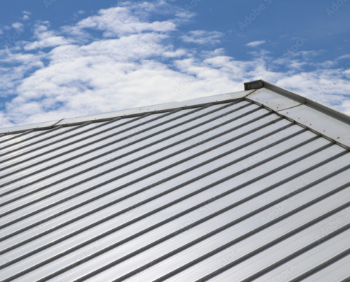 Standing seam metal roof and slope with clouds and blue sky background.