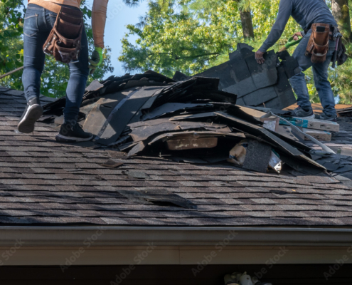 Roofers removing old material from a house in preparation for storm damage repair.
