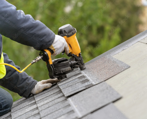 Workman using pneumatic nail gun install tile on roof of new house under construction