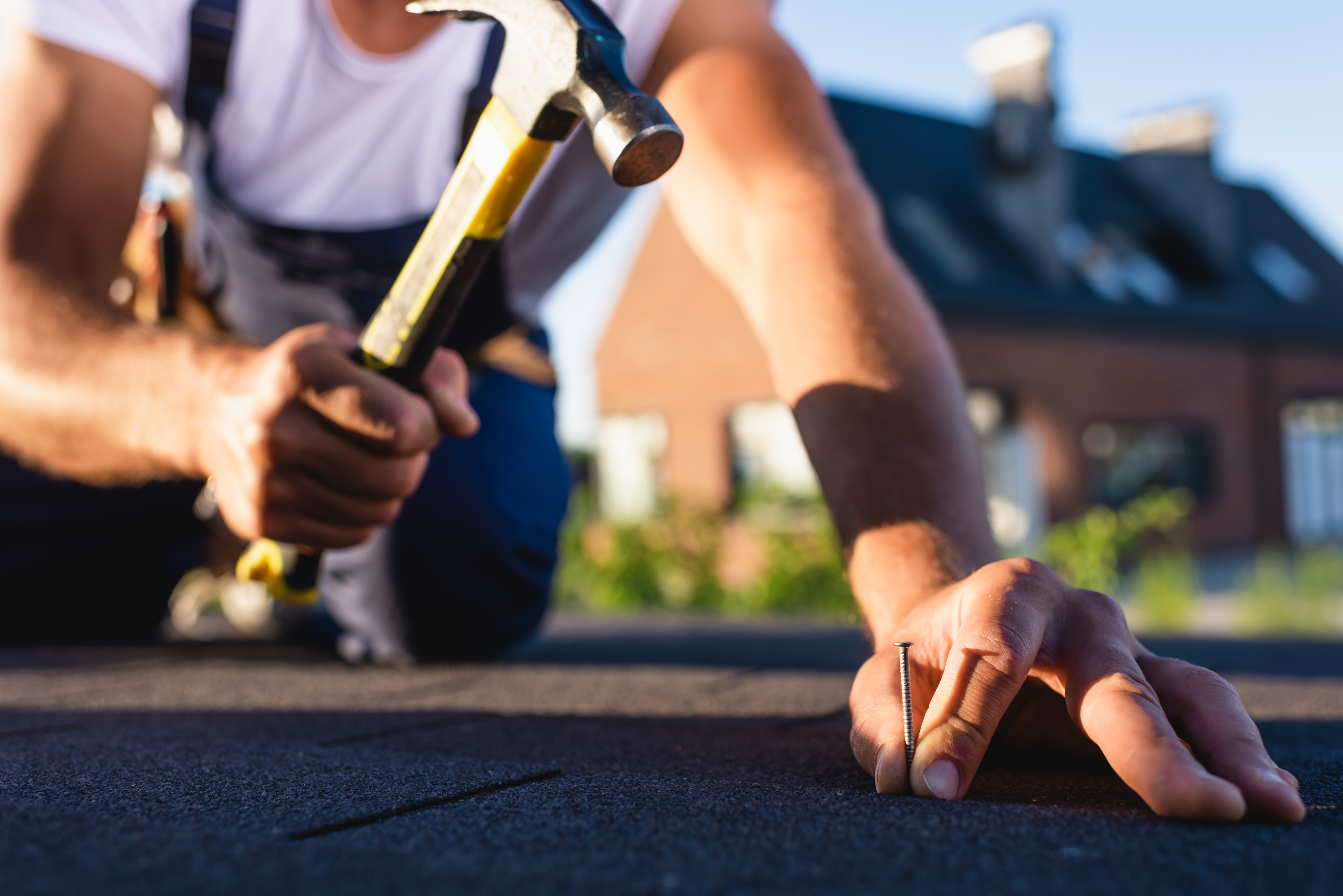 Close-up of a roofer hand-nailing replacement shingles during a roof repair in Dallas-Fort Worth