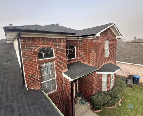 Aerial angle of a red brick two-story home with a newly completed dark shingle roof