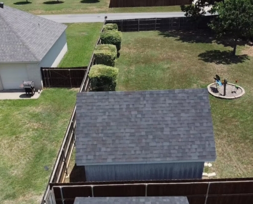 Aerial view of a backyard shed with a new gray shingle roof beside a metal-roofed section.
