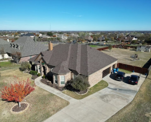 Aerial of a brick home with a new brown shingle roof in an open North Texas neighborhood