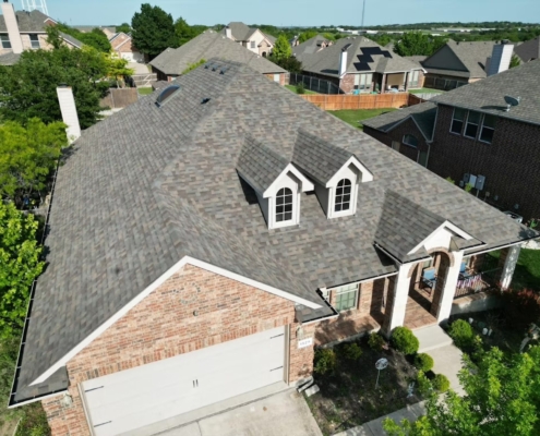 Aerial of a brick home's new textured shingle roof with two arched dormer windows