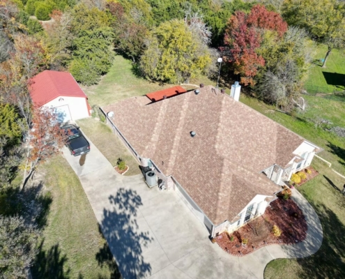 Aerial of a country home's new brown shingle roof with a red metal-roofed outbuilding