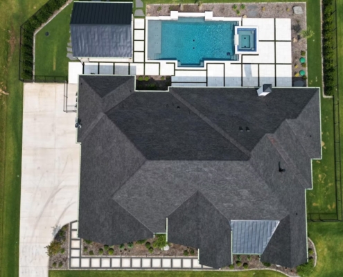 Aerial view of a large custom home's new charcoal shingle roof beside a backyard pool