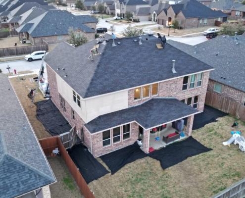 Overhead view of a large two-story brick home being reroofed with crew working and yards tarped off.