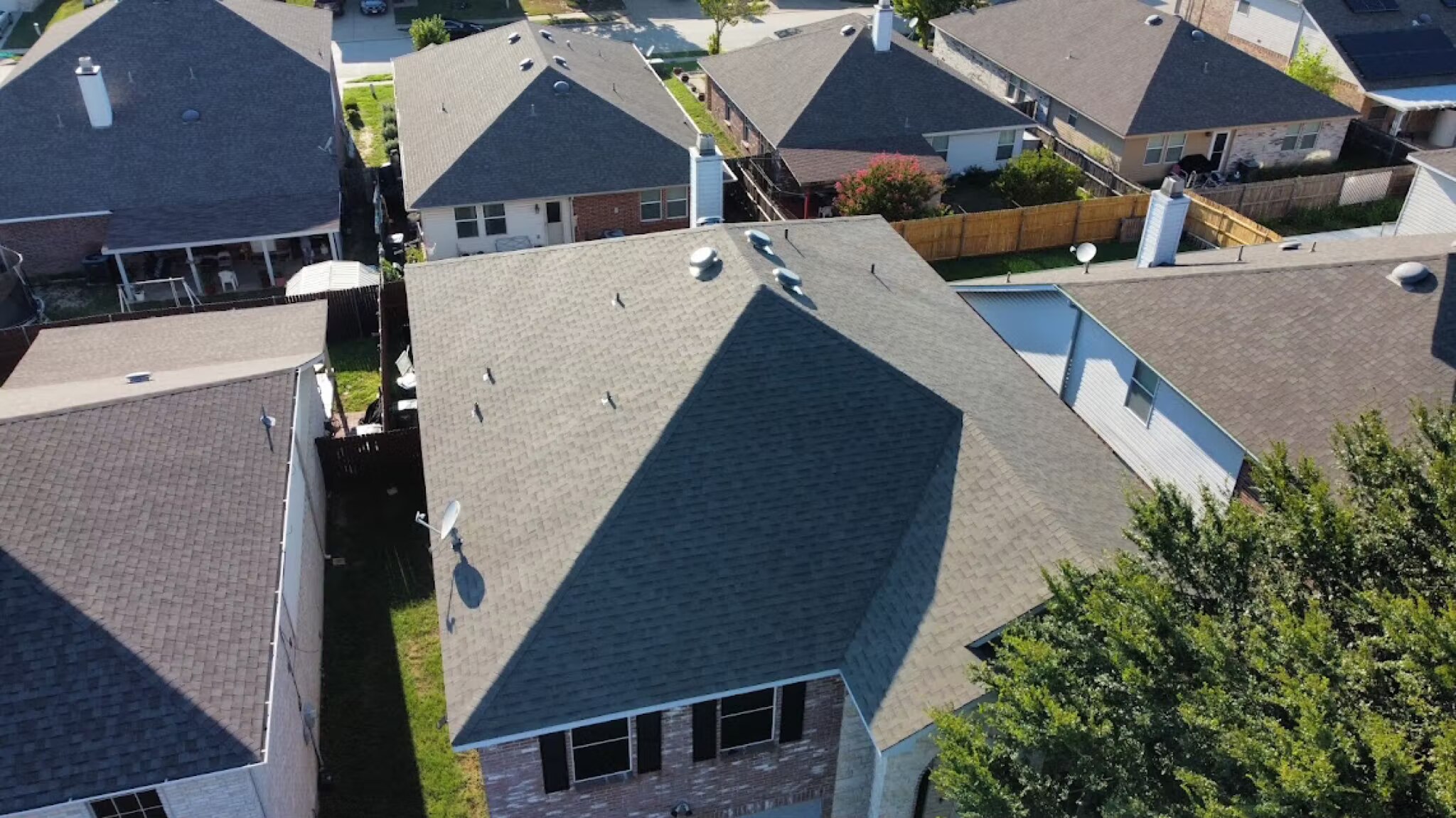 Drone view of a completed gray shingle roof among homes in a North Texas neighborhood