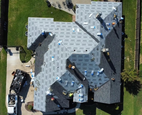 Aerial of a large roof mid-installation with underlayment down and stacked shingle bundles
