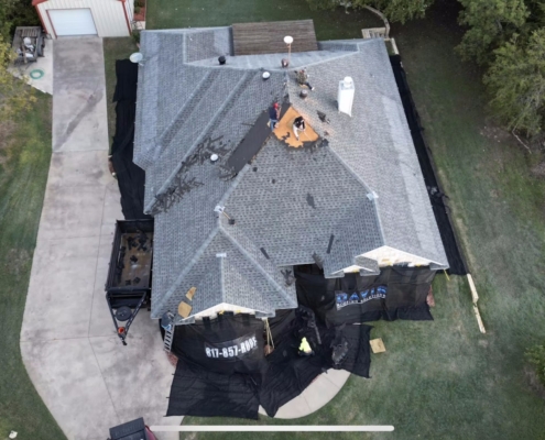 Aerial of a shingle roof replacement underway with the crew at the ridge and a loaded debris trailer.