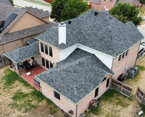 Aerial of a two-story brick home with a freshly installed charcoal shingle roof