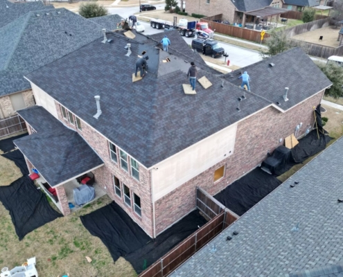 Overhead view of a crew stripping and replacing shingles on a large two-story brick home.