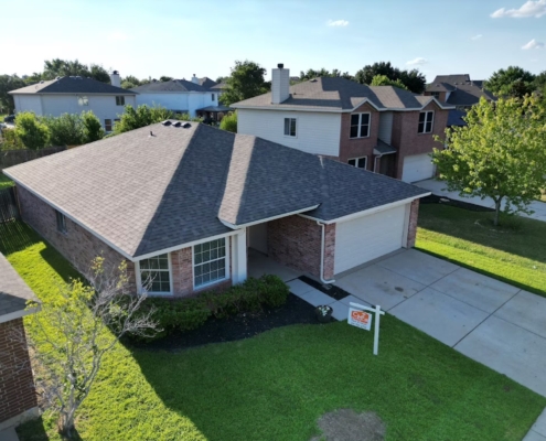 Aerial view of a two-story brick home showing a new gray shingle roof and attached garage.