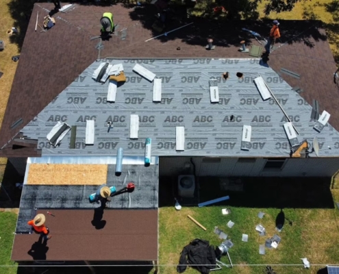 Aerial of a roof mid-replacement with synthetic underlayment down and crew working the deck