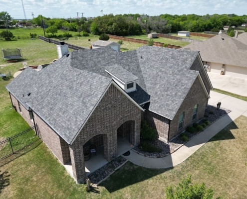 Aerial of a brick home with a newly completed gray shingle roof on a large lot