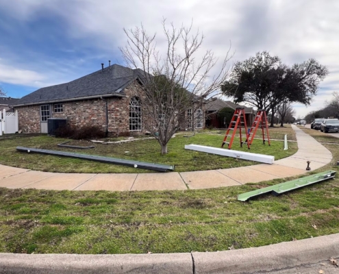 Brick home with a dark shingle roof and new gutter sections staged on the lawn before installation.