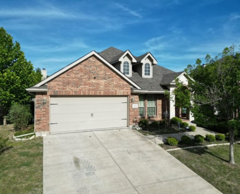 Two-story brick home showing a completed architectural shingle roof under a clear blue sky