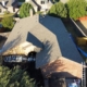 Aerial view of a finished charcoal shingle roof with a roofing banner hung on the home below