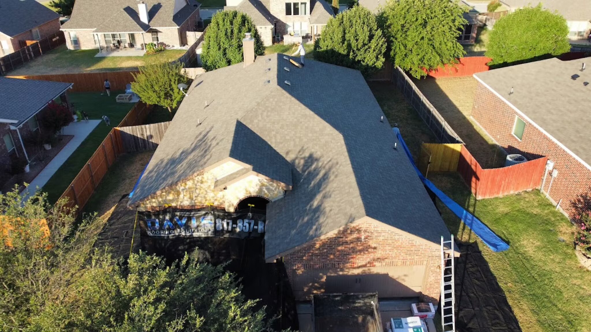 Aerial view of a finished charcoal shingle roof with a roofing banner hung on the home below