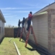 Roofing crew on ladders installing fascia and drip edge along the eave of a home