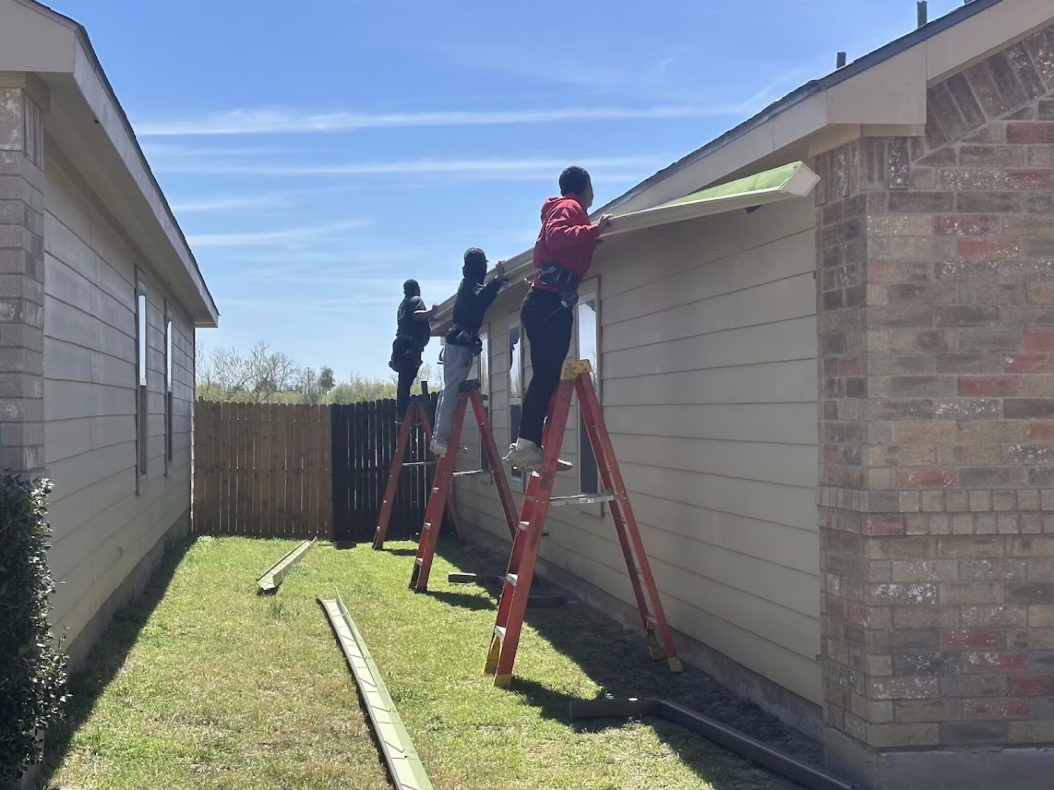 Roofing crew on ladders installing fascia and drip edge along the eave of a home