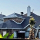 Roofing crew installing shingles over synthetic underlayment on a brick home with a ladder in place