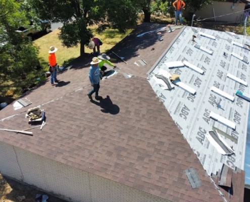 Roofing crew installing shingles and underlayment on a single-story home, seen from above