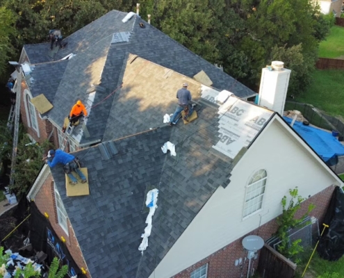 Aerial of a roofing crew replacing shingles on a two-story home with fresh decking exposed