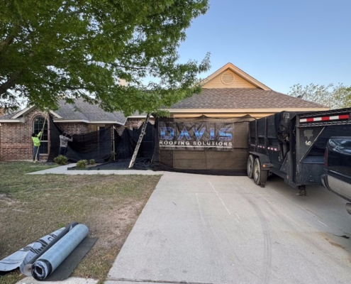 Roofing crew setting protective tarps around a home with a dump trailer in the driveway