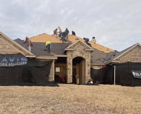 Roofing crew replacing shingles on a stone home with Davis Roofing banners across the front