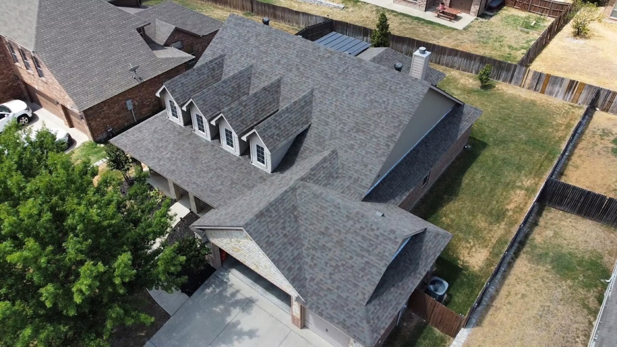 Aerial of a finished shingle roof with four dormers on a large brick home