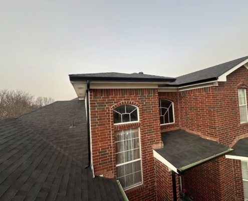 Elevated view of fresh dark shingles across the roof of a two-story red brick home