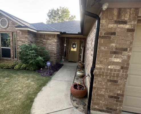 Brick home entryway with a new dark shingle roof and a fresh black gutter downspout.