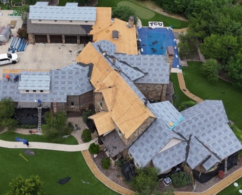 Aerial of a large estate mid roof replacement with crews and exposed decking across several sections