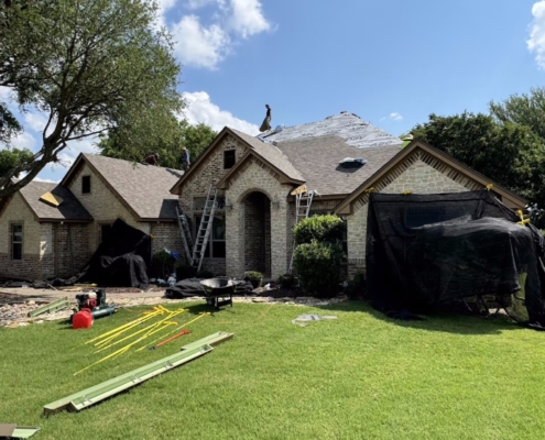 Large brick and stone home mid re-roof with synthetic underlayment exposed and ladders on the eaves.