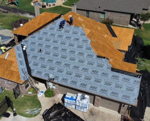 Aerial of a home mid-reroof with underlayment installed and roofers working near the ridge