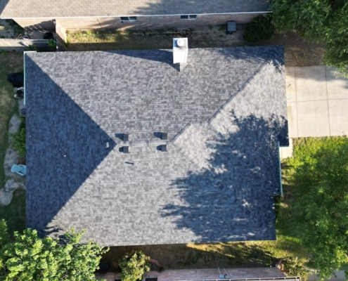 Overhead drone shot of a freshly shingled hip roof with ridge vents and a chimney.