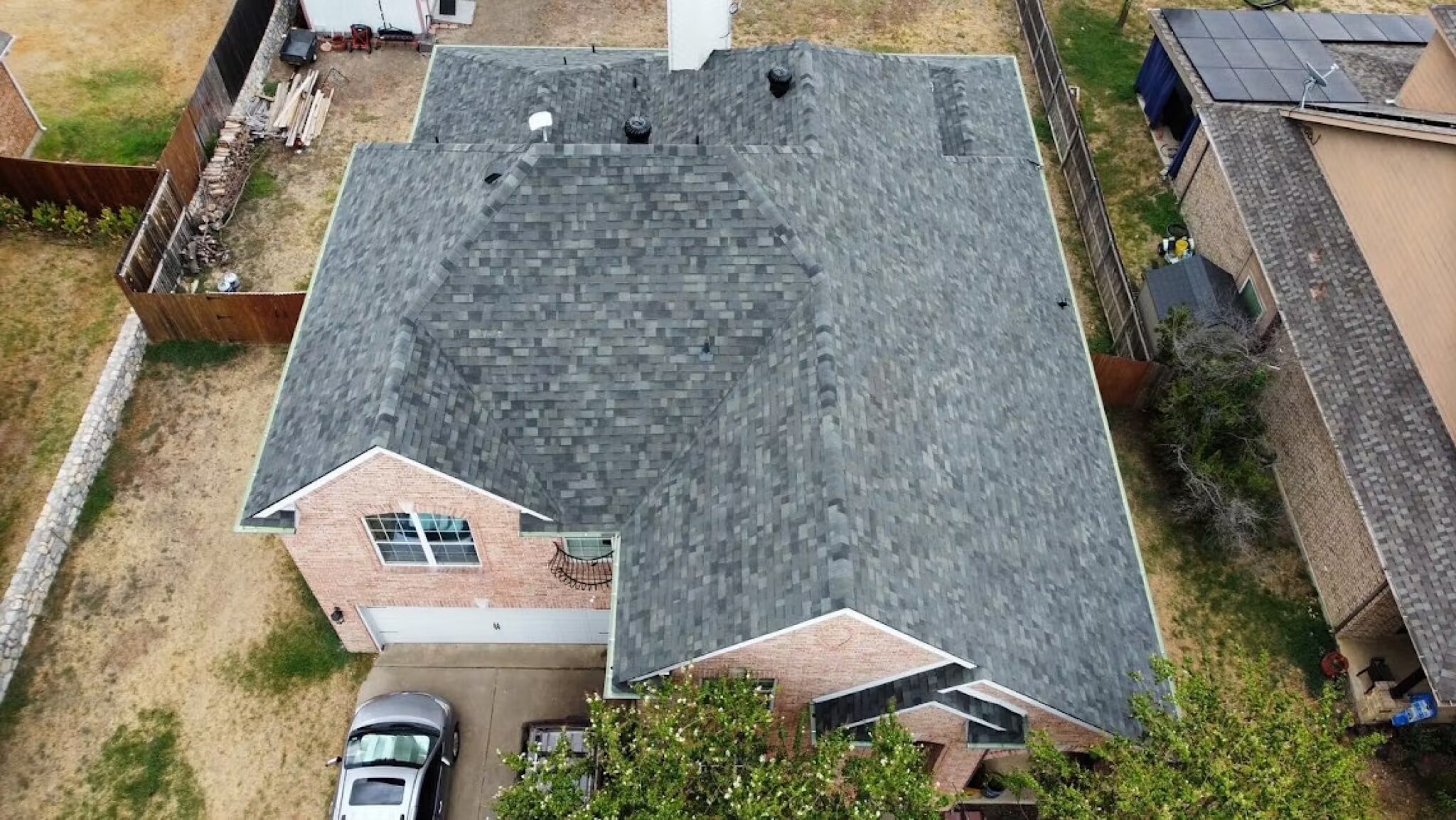 Top-down aerial of a completed slate-gray shingle roof with attic vents