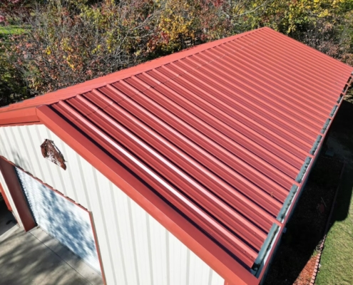 New red metal roof with standing ribs installed on a white steel workshop building