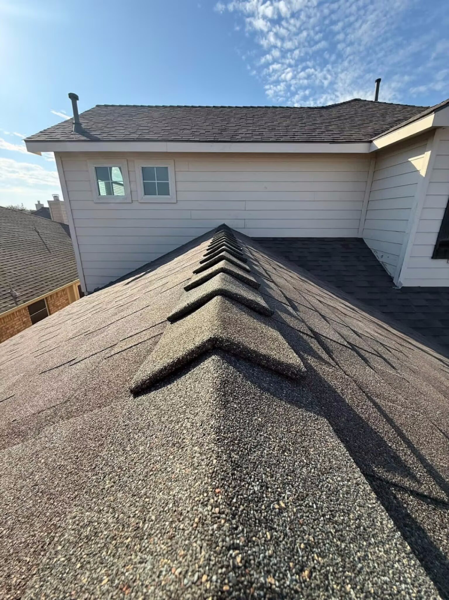 Close view of new ridge-cap shingles running along the peak of a freshly roofed home
