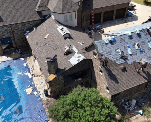 Overhead view of a roof replacement in progress with synthetic underlayment and shingle bundles staged