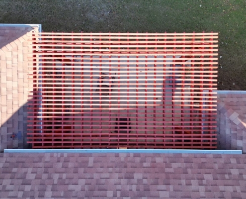 Overhead view of new shingle roof planes flanking a red slatted pergola above a patio.