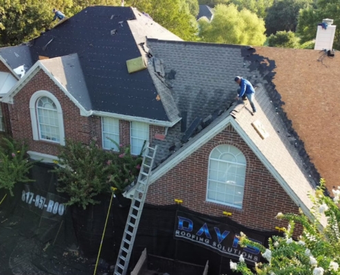 Aerial of a worker stripping old shingles on a brick home with a Davis Roofing banner hung below