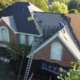 Aerial of a worker stripping old shingles on a brick home with a Davis Roofing banner hung below