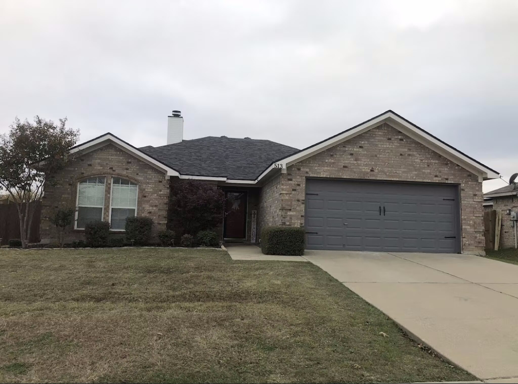 Front exterior of a single-story brick home with a new dark shingle roof on a cloudy day