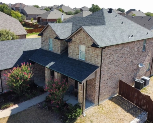 Drone view of a stone-and-brick home with a newly finished gray shingle roof in a DFW neighborhood