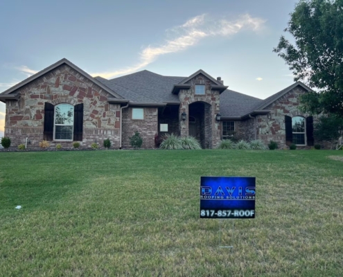 Stone home at dusk with a finished shingle roof and a Davis Roofing yard sign out front
